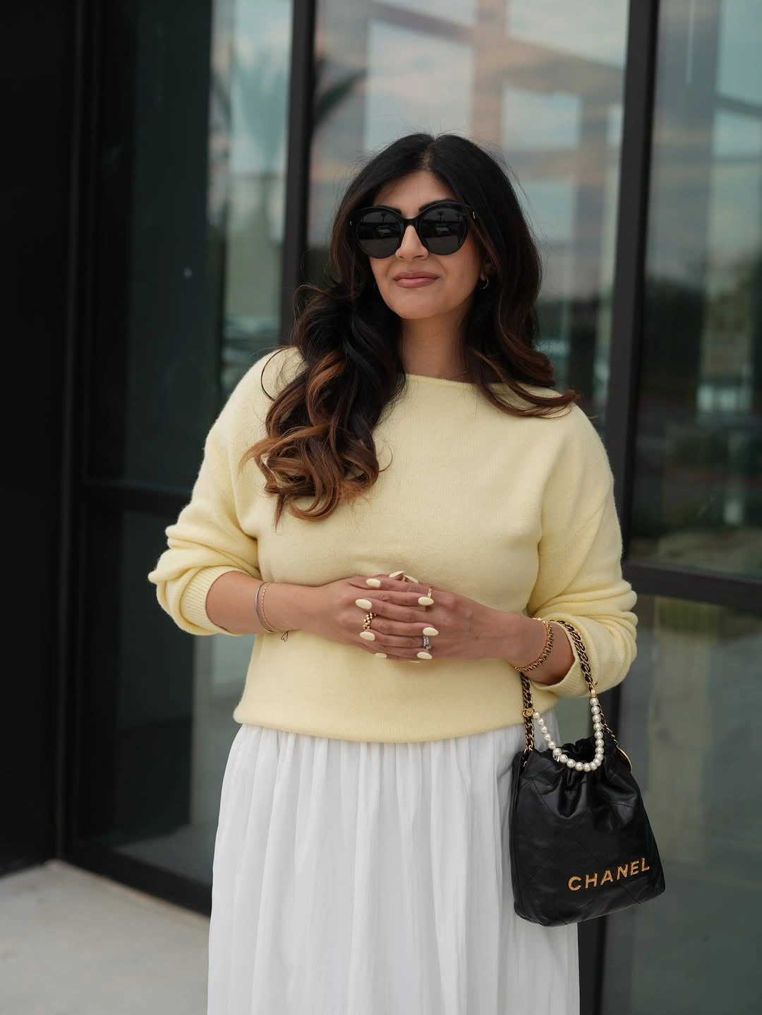 Pale yellow sweater with white pleated skirt and black handbag