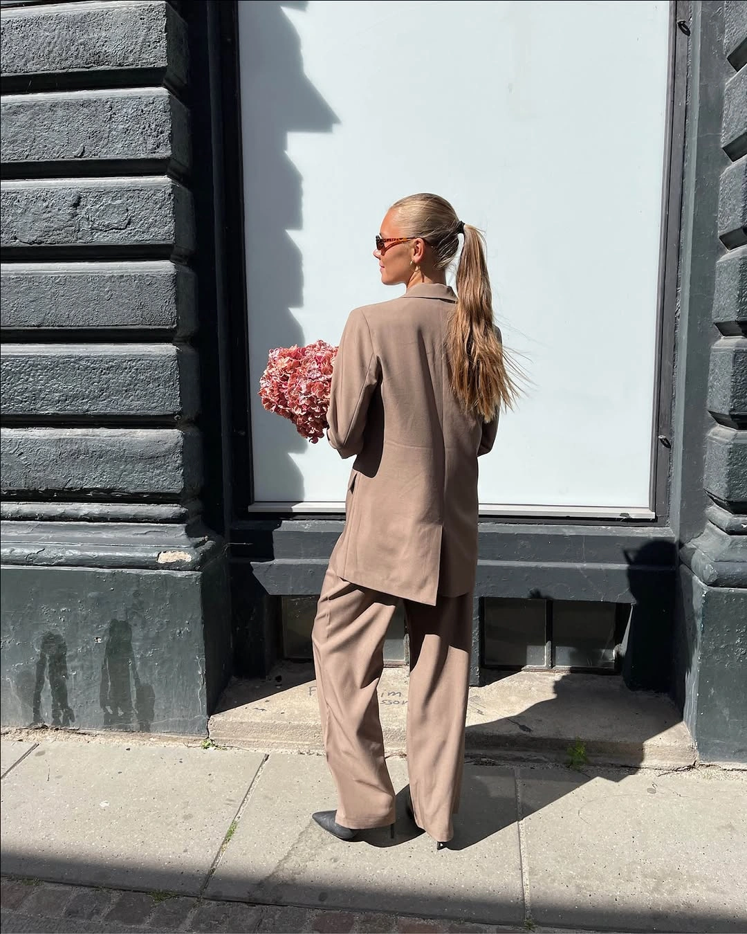 Long taupe-brown blazer with wide-leg trousers and dark pointed shoes