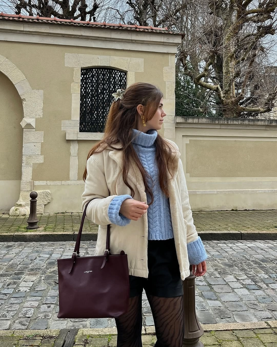 pale blue cable knit with light coat black shorts tights and burgundy tote