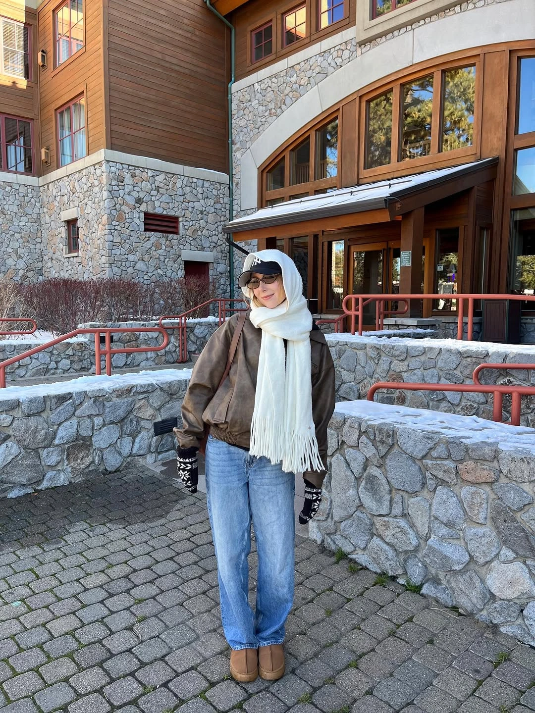 Brown jacket with wide white scarf, jeans, cap, and gloves