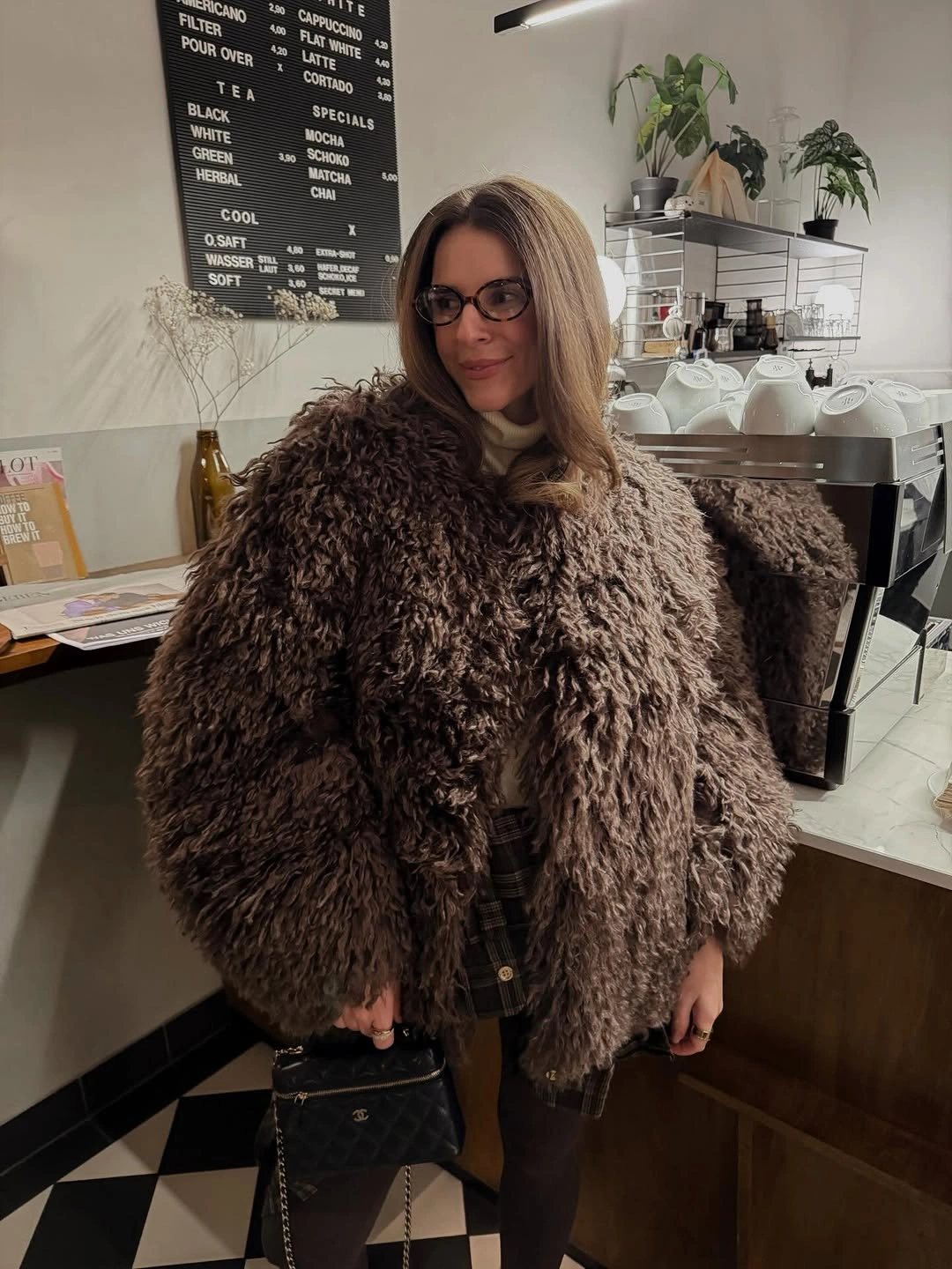 Brown textured-looking jacket with plaid skirt-like layer and black bag