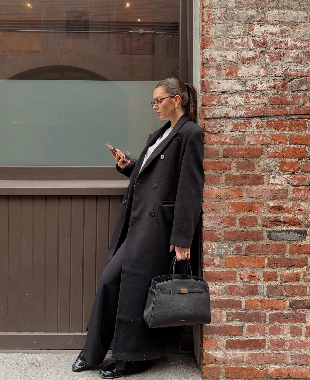 Long black double-breasted coat with wide trousers and structured handbag