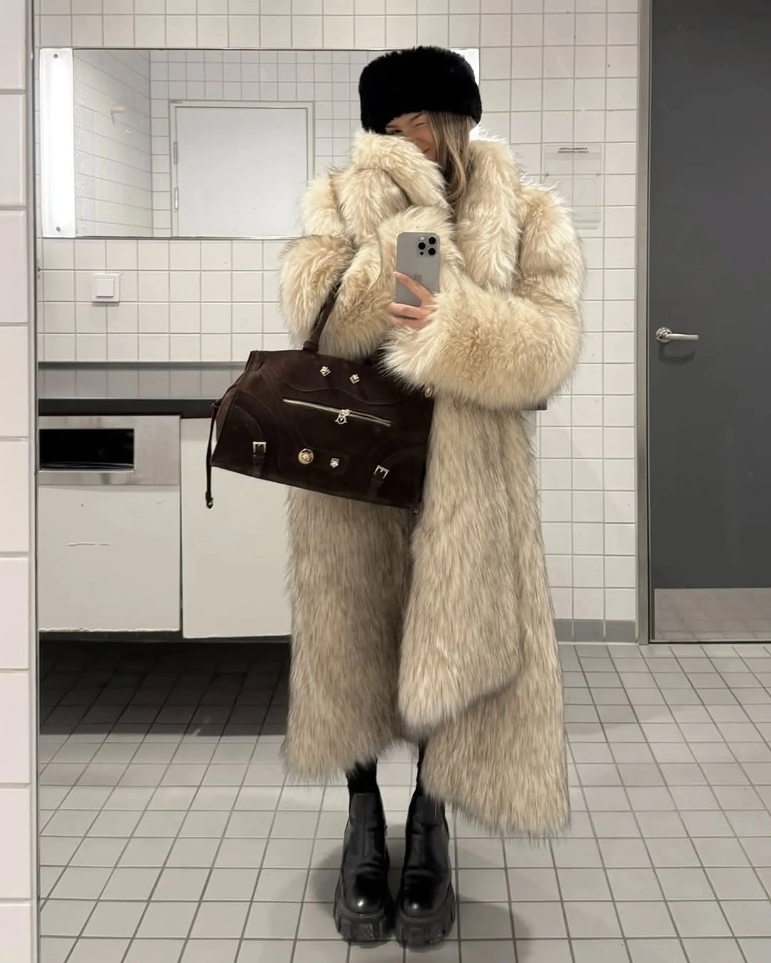 Cream fuzzy-looking long coat with black hat, bag, and boots