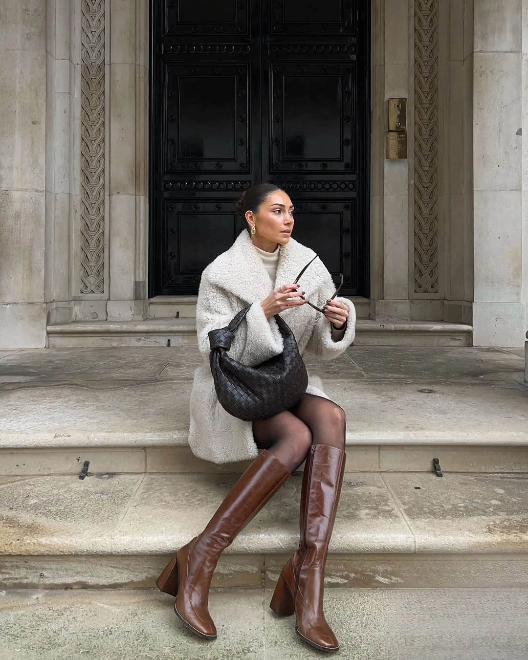 Cream textured-looking coat with brown boots and black woven-looking bag