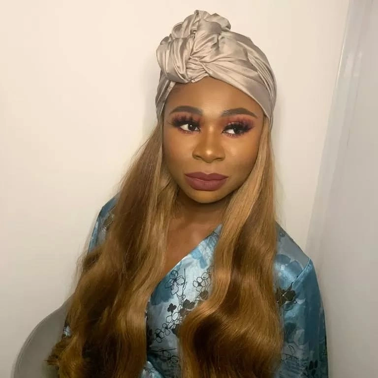 Long honey blonde waves under pale wrapped head covering