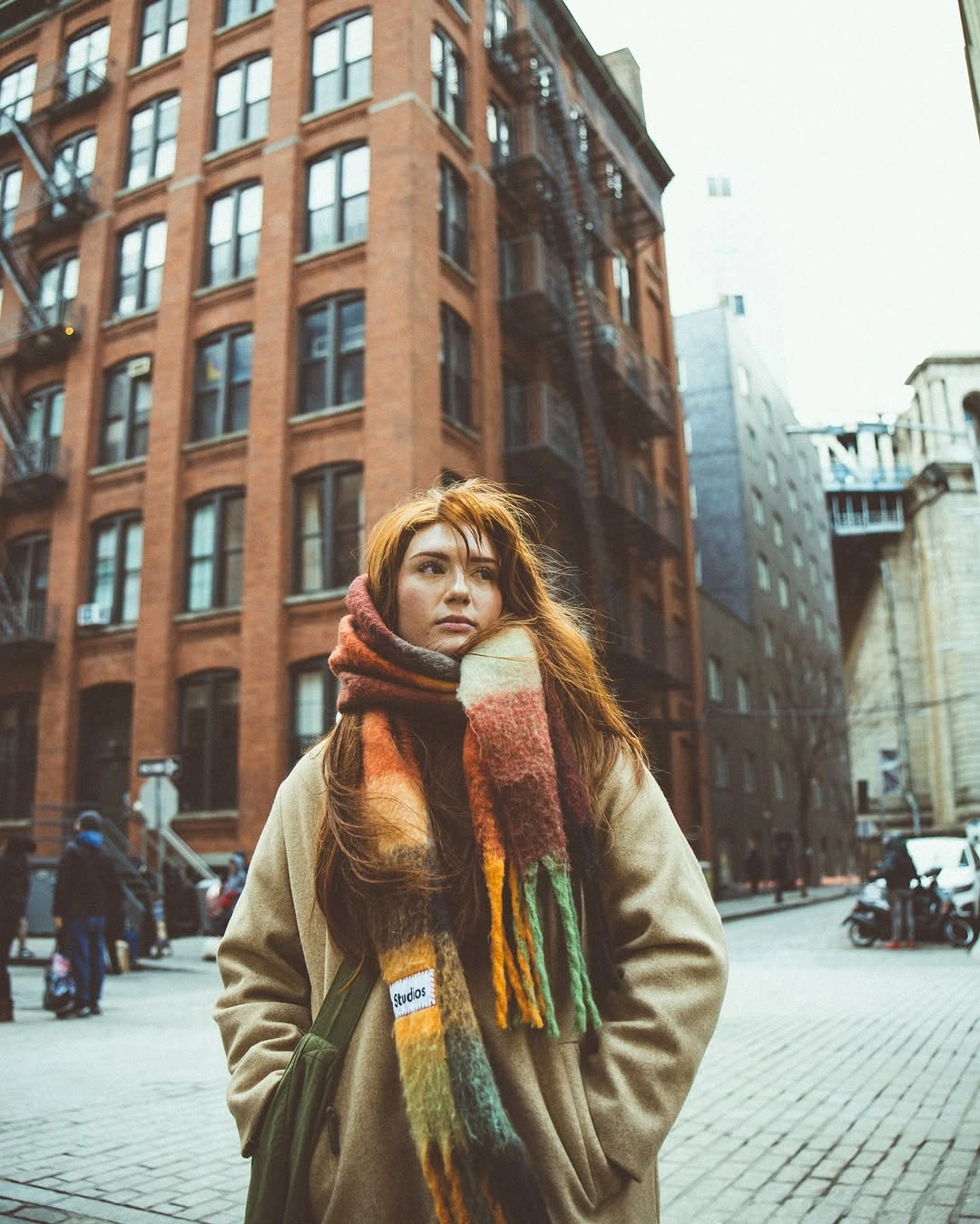 Woman in neutral coat with oversized multicolor plaid fringed scarf