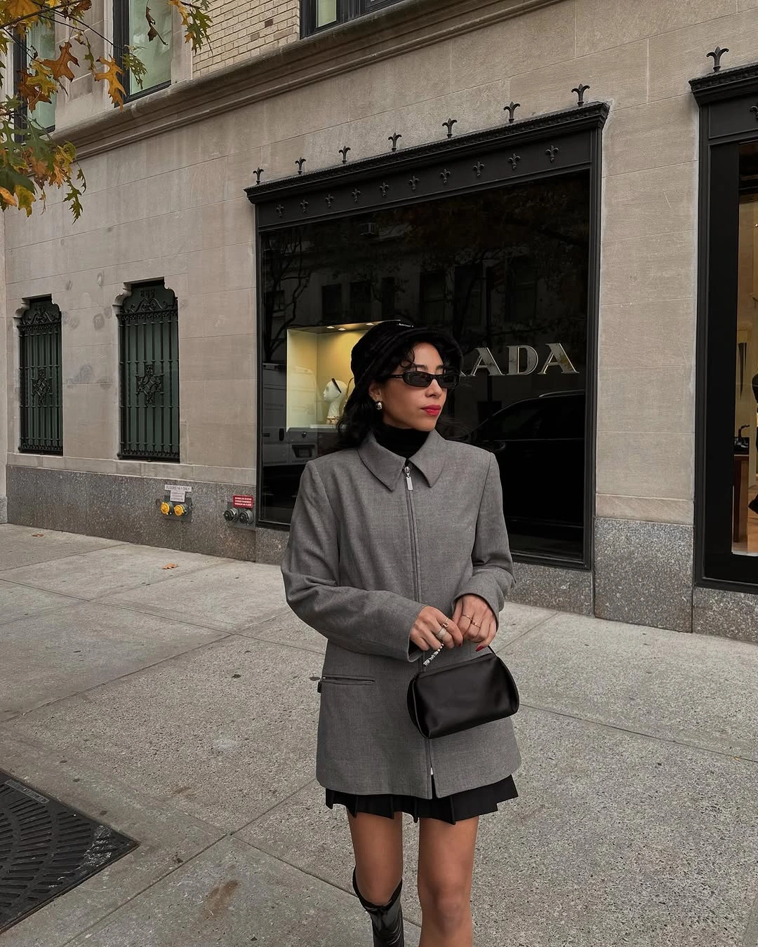 Woman in gray jacket, black pleated skirt, beret, and tall boots