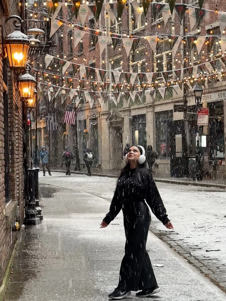 Woman in long black ensemble with white earmuffs on snowy street