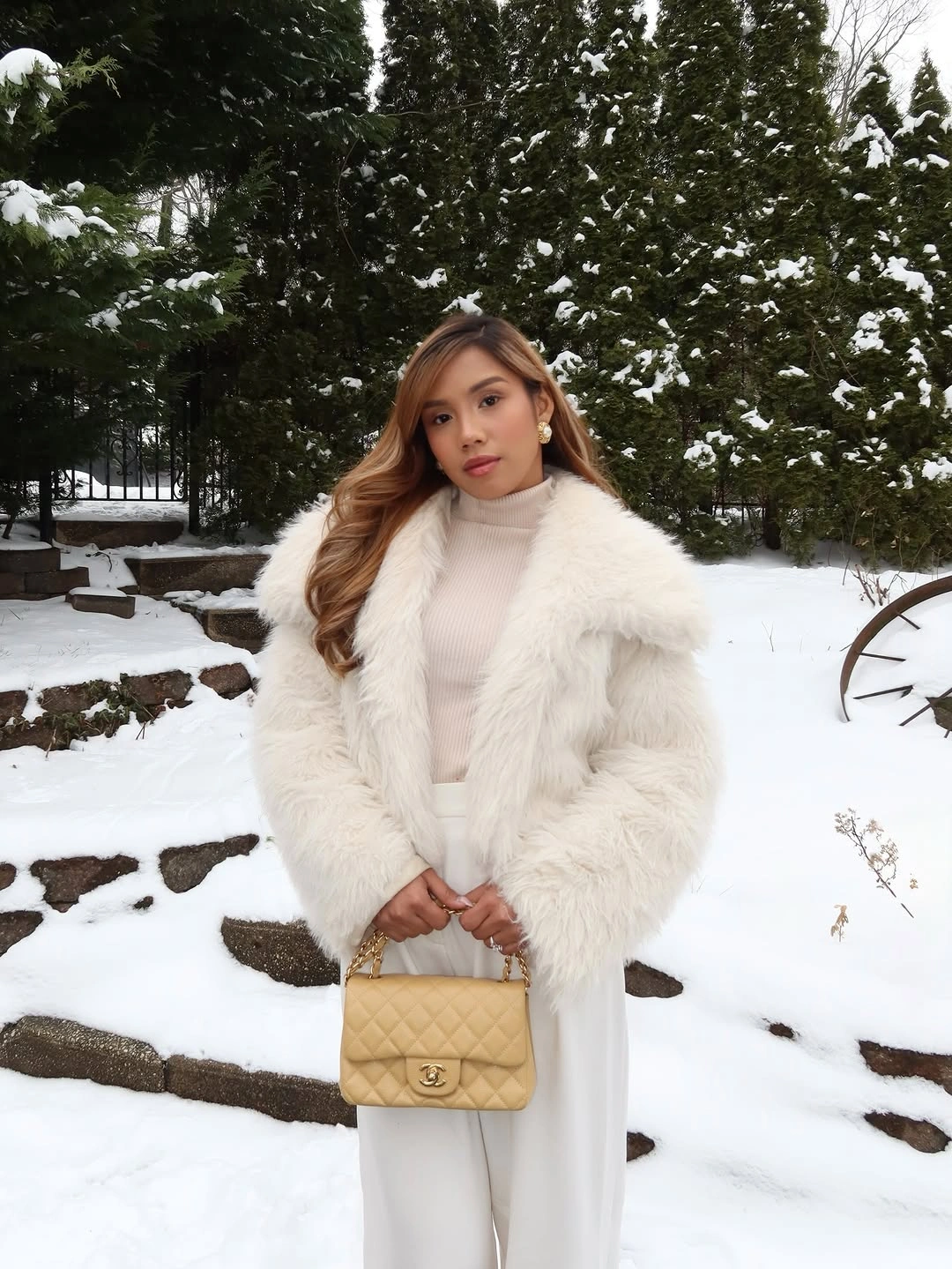 Woman in white fur-looking jacket, cream turtleneck, and white trousers