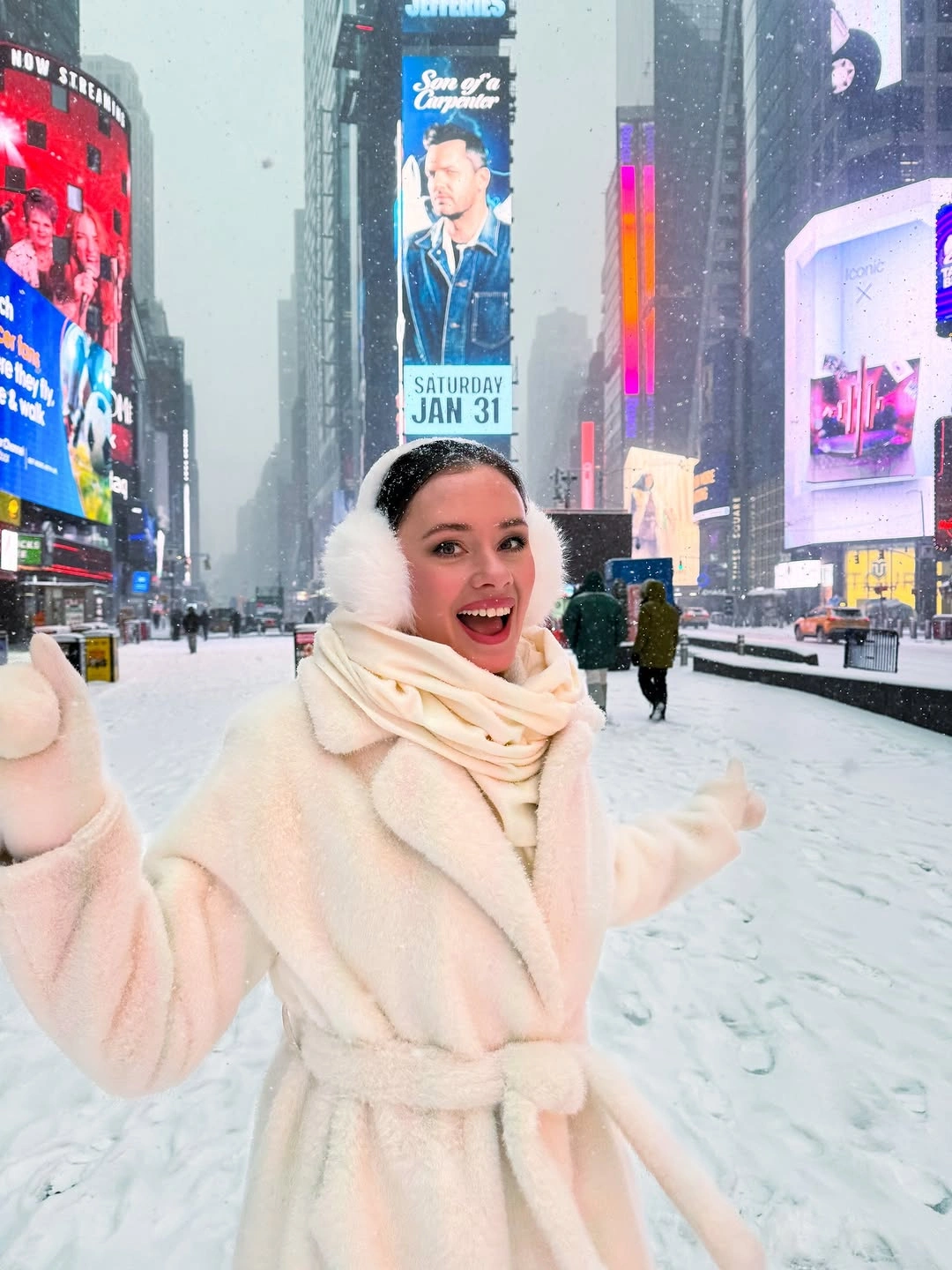 Woman in pale belted coat, cream scarf, and white earmuffs