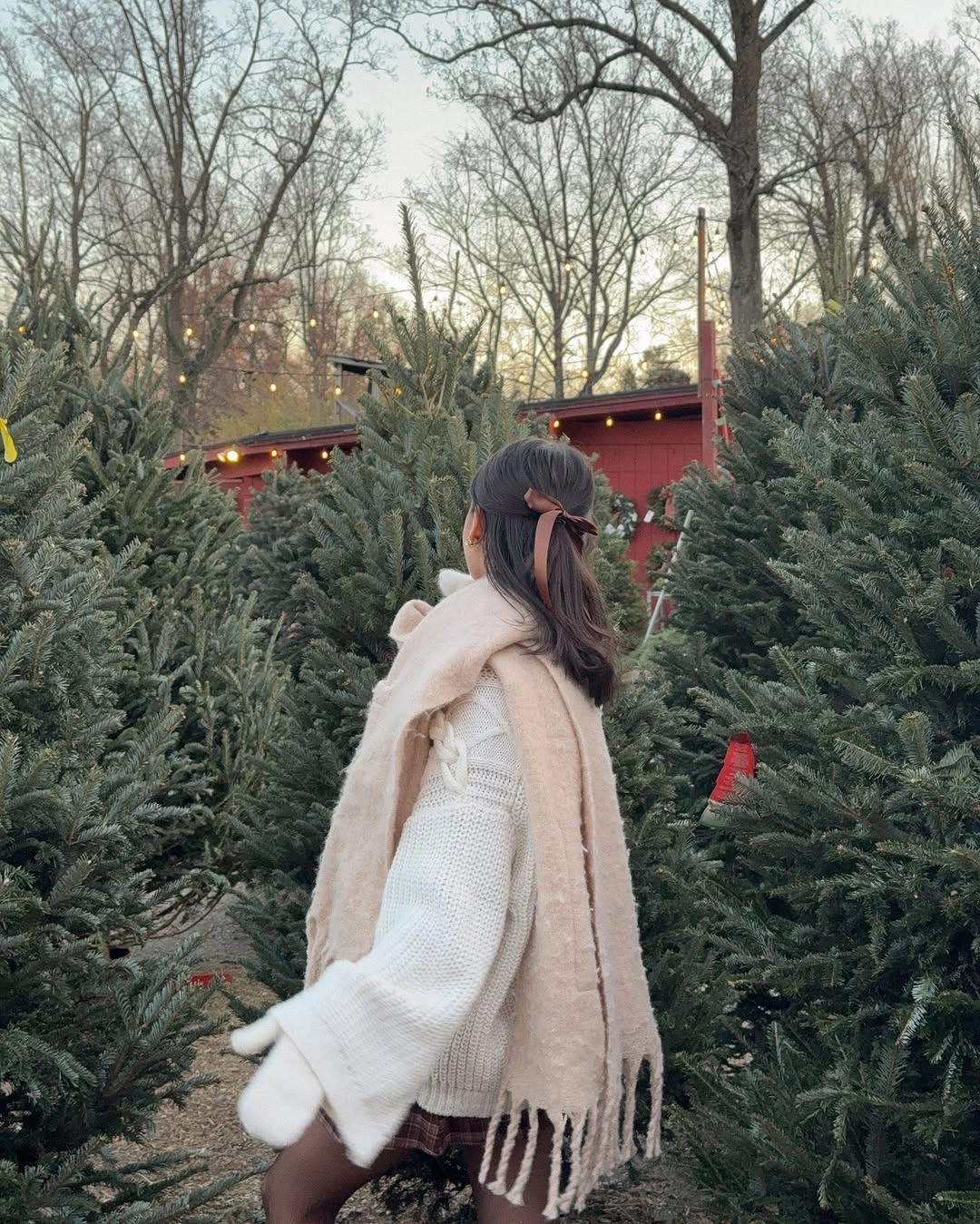 Woman in cream sweater, fringed scarf, plaid skirt, and mittens