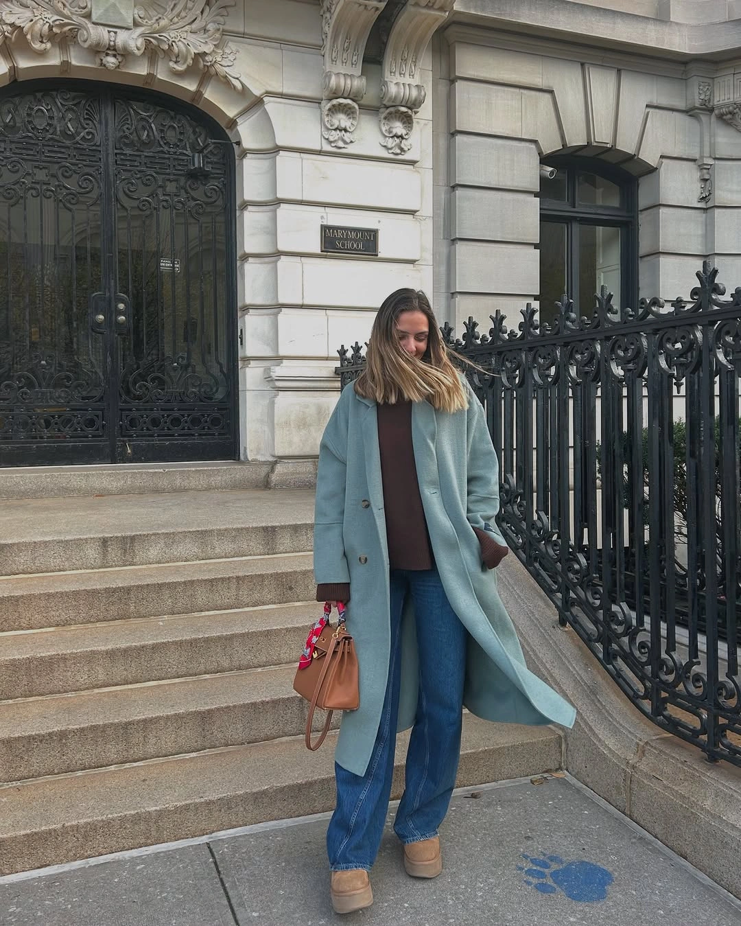Woman in pale blue coat, brown top, jeans, and tan shoes