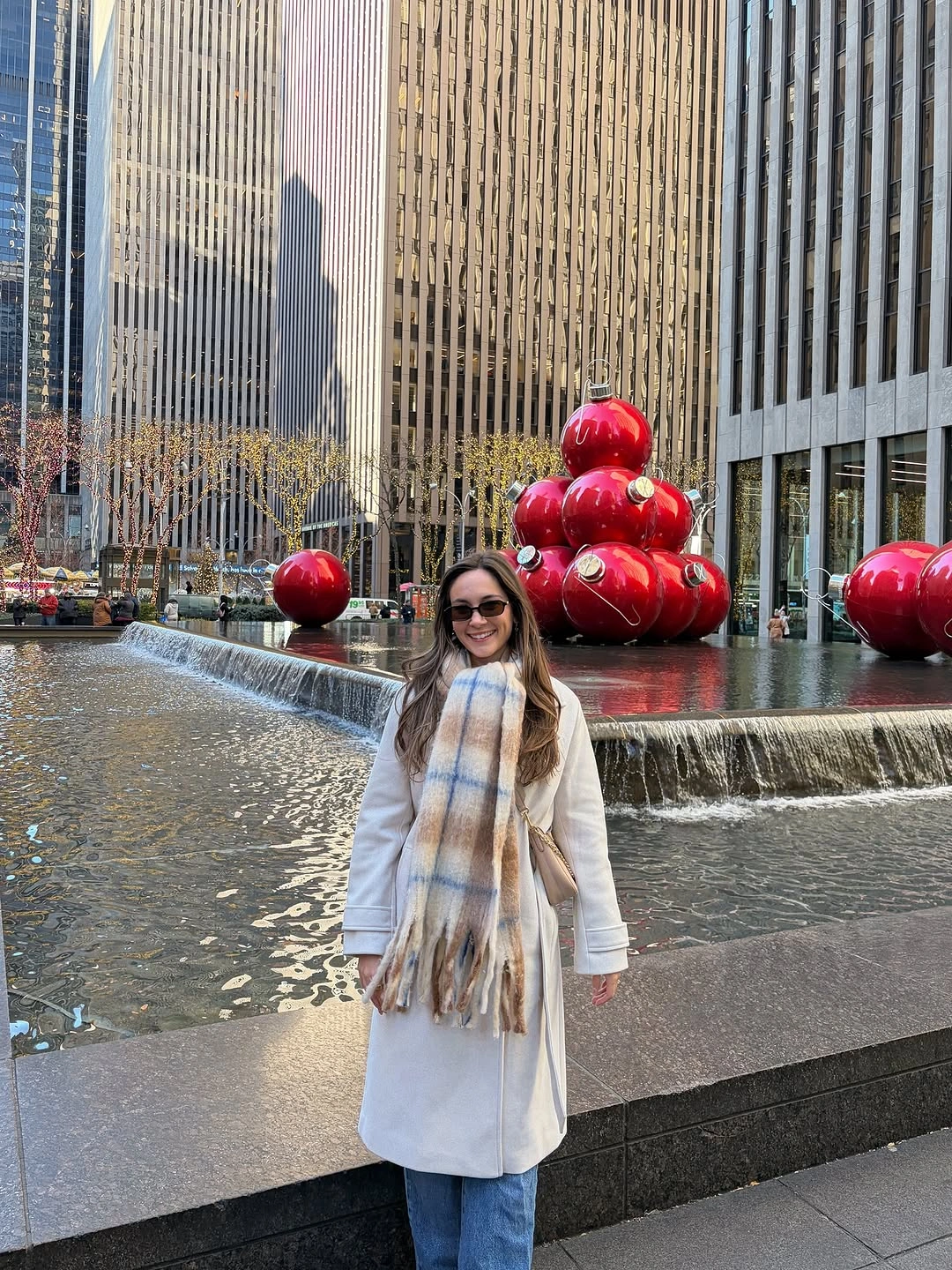 Woman in white coat, blue jeans, plaid scarf, and sunglasses