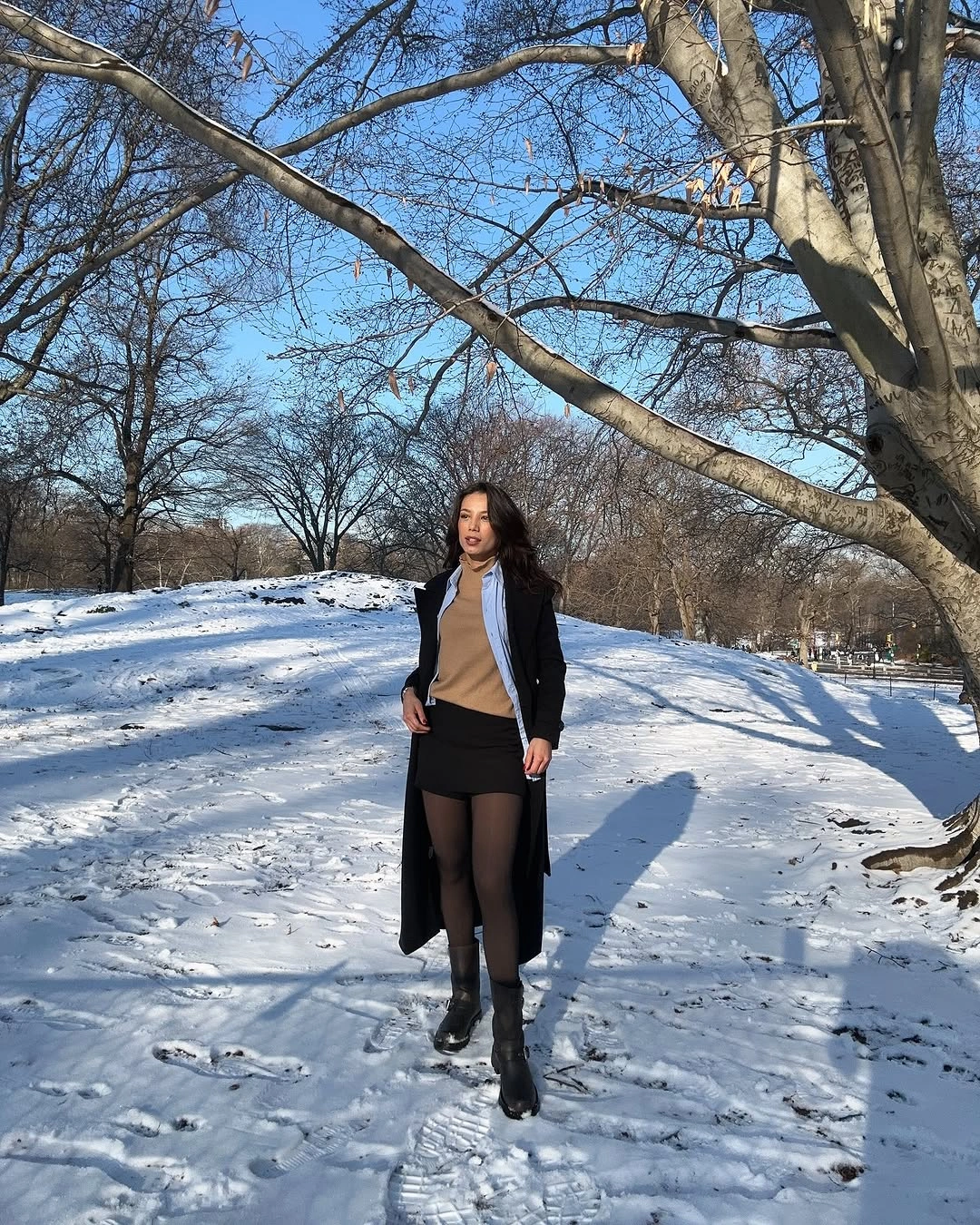 Woman in long black coat, short skirt, tights, and ankle boots