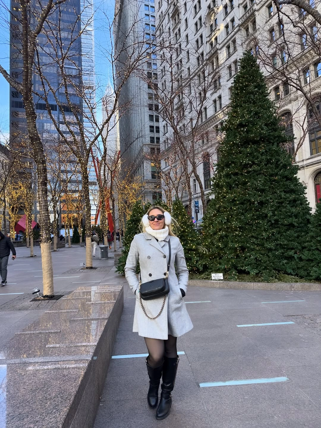 Woman in gray coat, white scarf, earmuffs, black tights, and boots