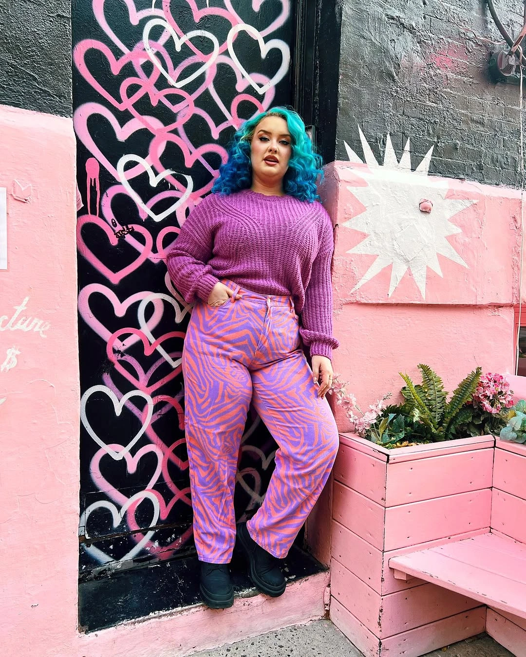Purple sweater, pink patterned trousers, black boots and teal hair