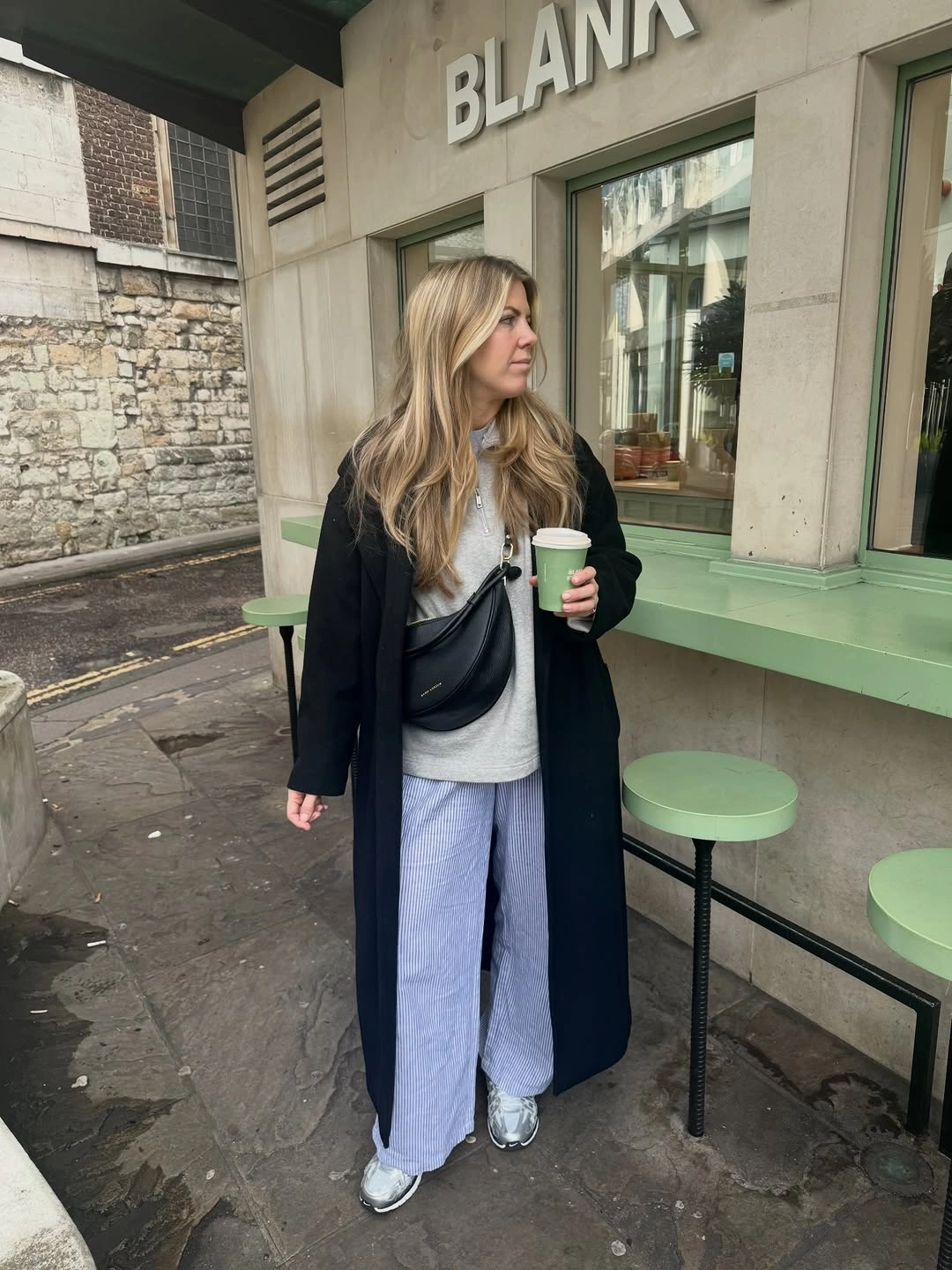 Long black coat with pale trousers and silver-toned sneakers