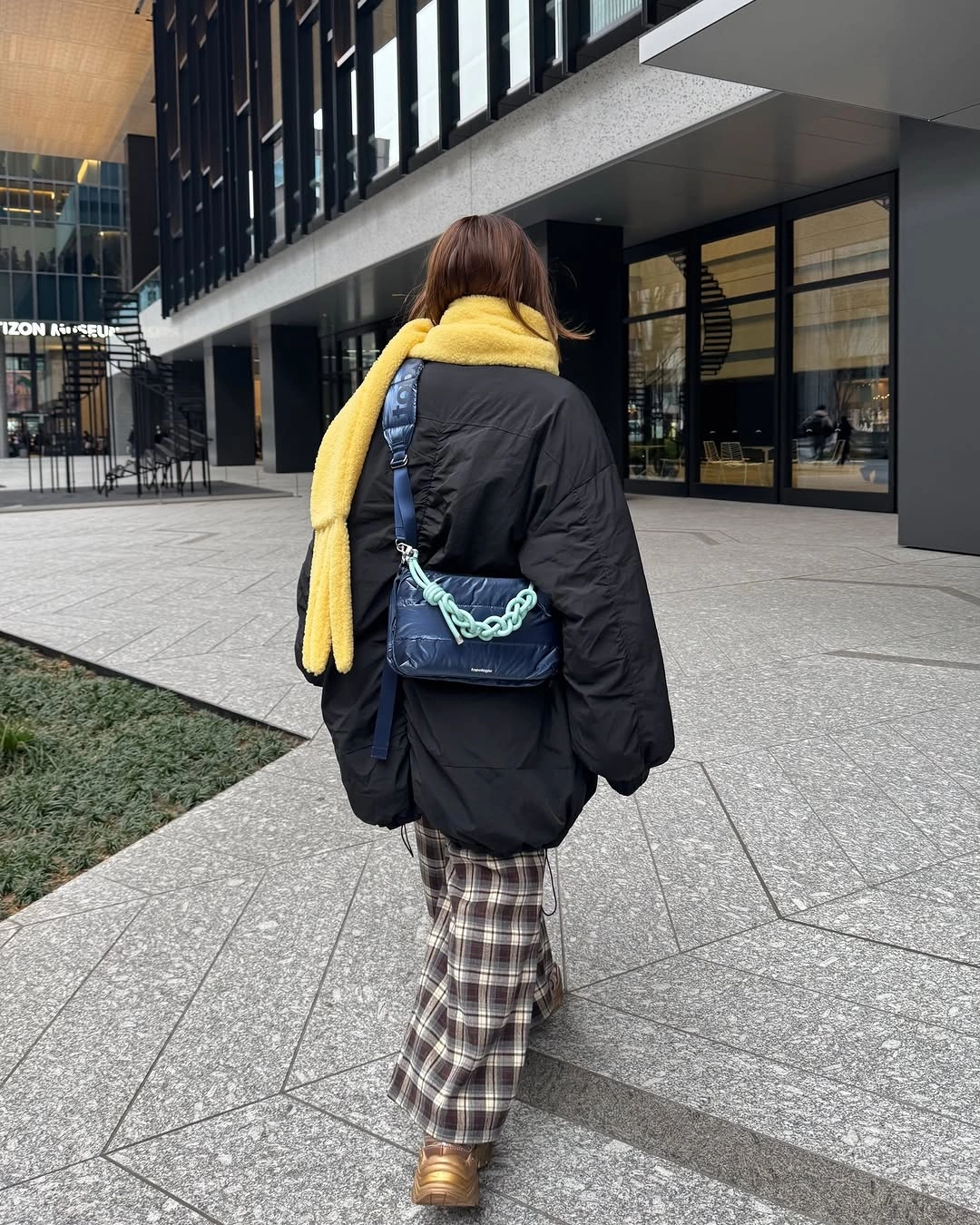 Back view with black jacket, yellow scarf, and checked trousers