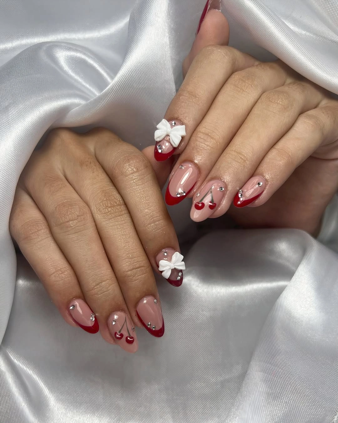 Nude-pink nails with red tips, rhinestones and white accents