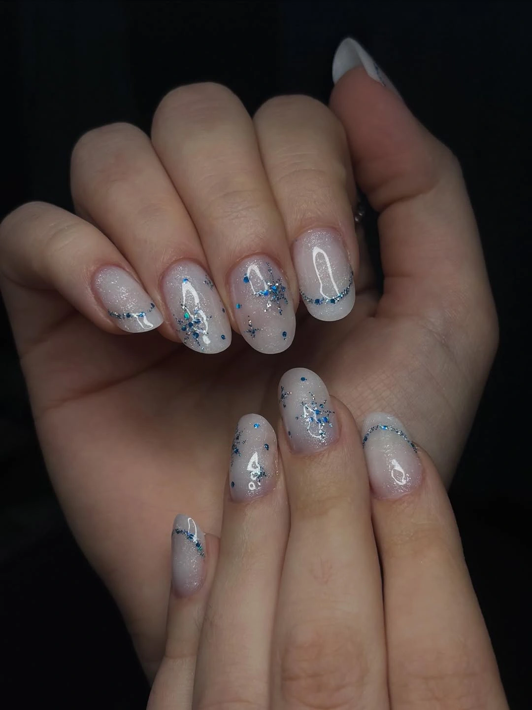 Milky rounded nails with blue glitter flecks and curved arcs