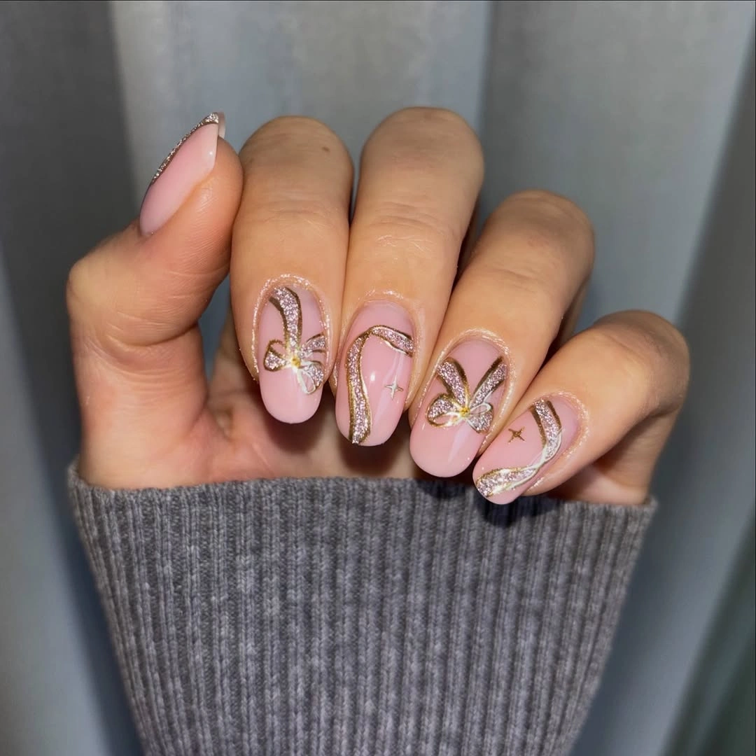 Pale pink almond nails with champagne glitter curves and bow-like accents