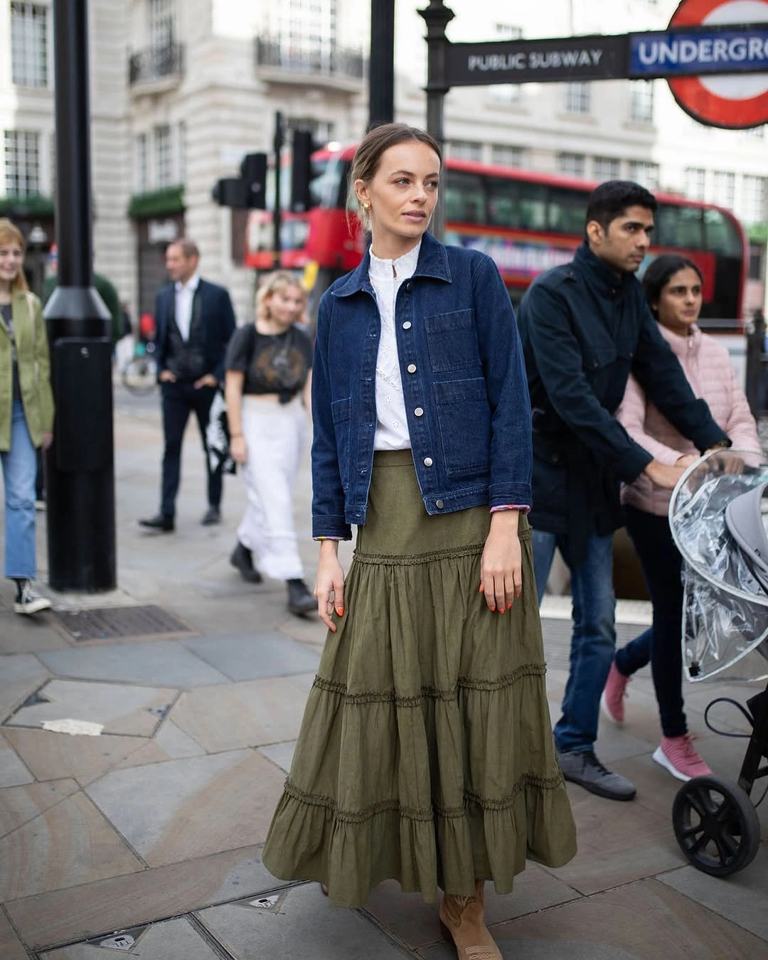 Blue denim-looking jacket with white top, olive tiered skirt, and boots