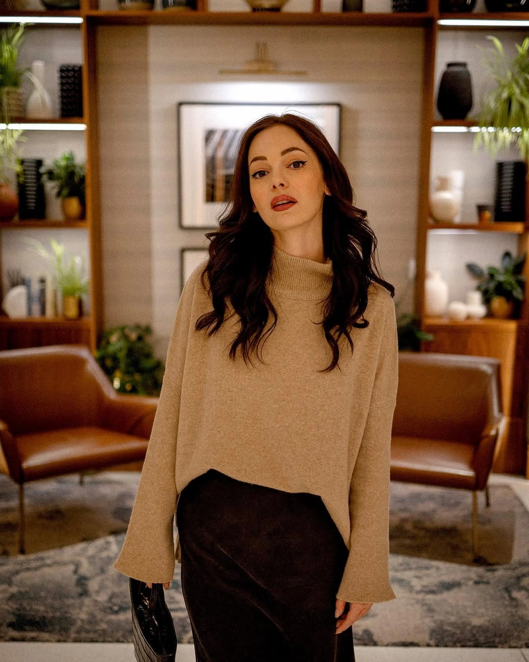 Beige high-neck sweater with satin-looking dark skirt and black boots