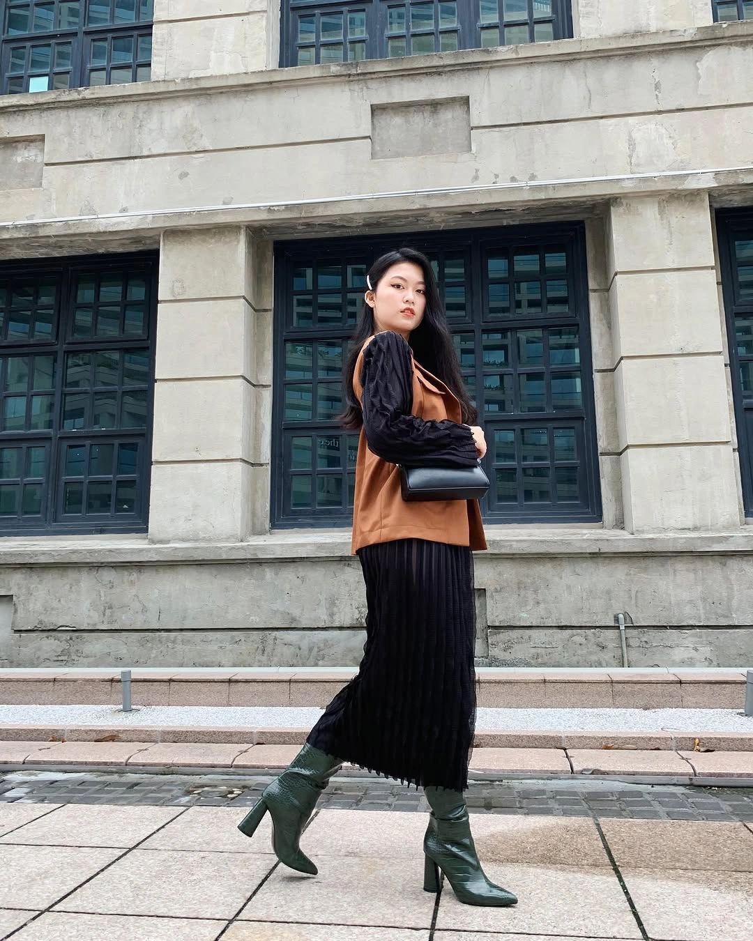Rust sleeveless layer over black top, long pleated-looking skirt, green boots