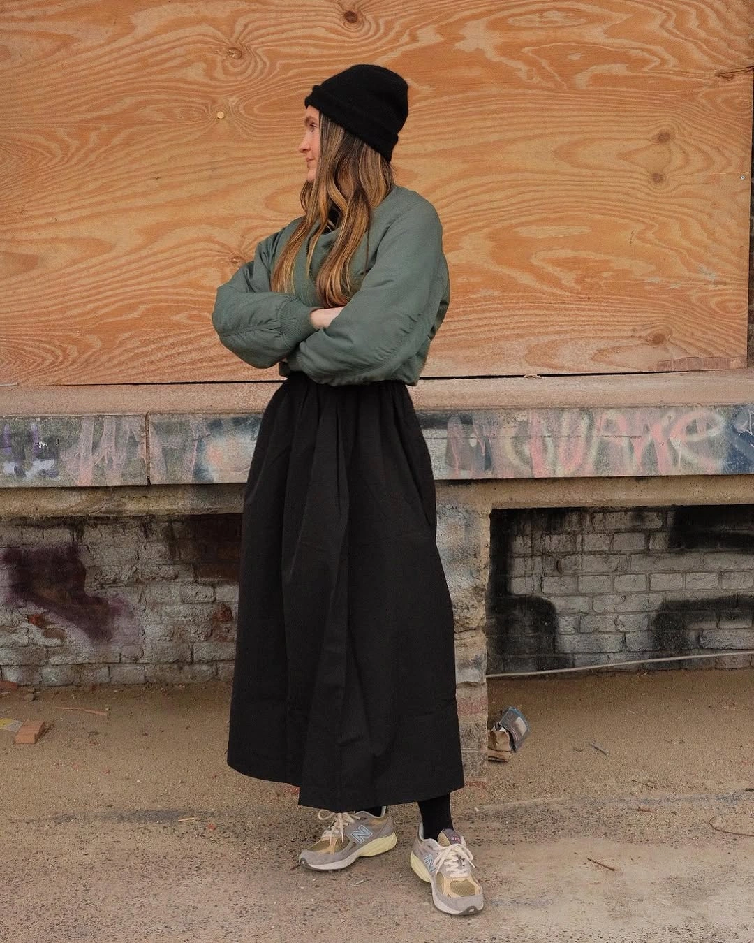 Green sweatshirt with long black gathered skirt, beanie, and gray sneakers