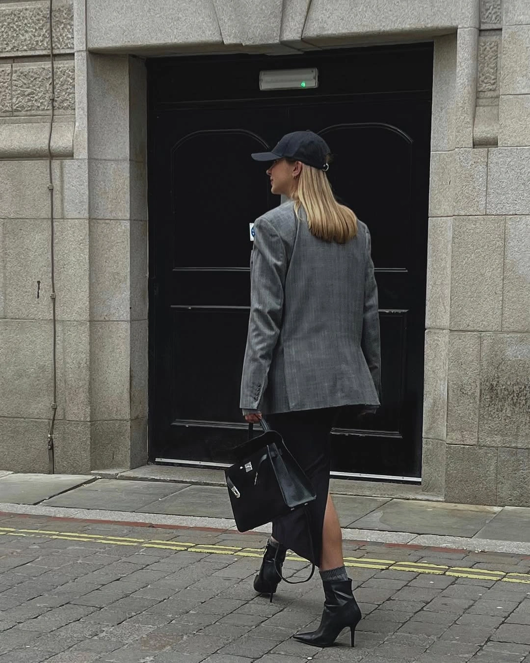 Gray blazer with black cap, slit black skirt, boots, and handbag