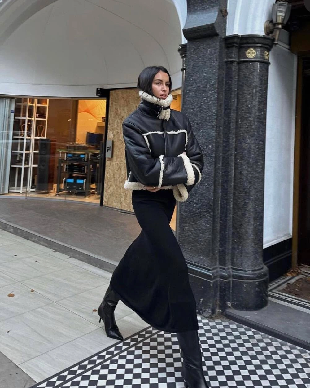 Black cropped jacket with cream textured-looking trim, long skirt, tall boots