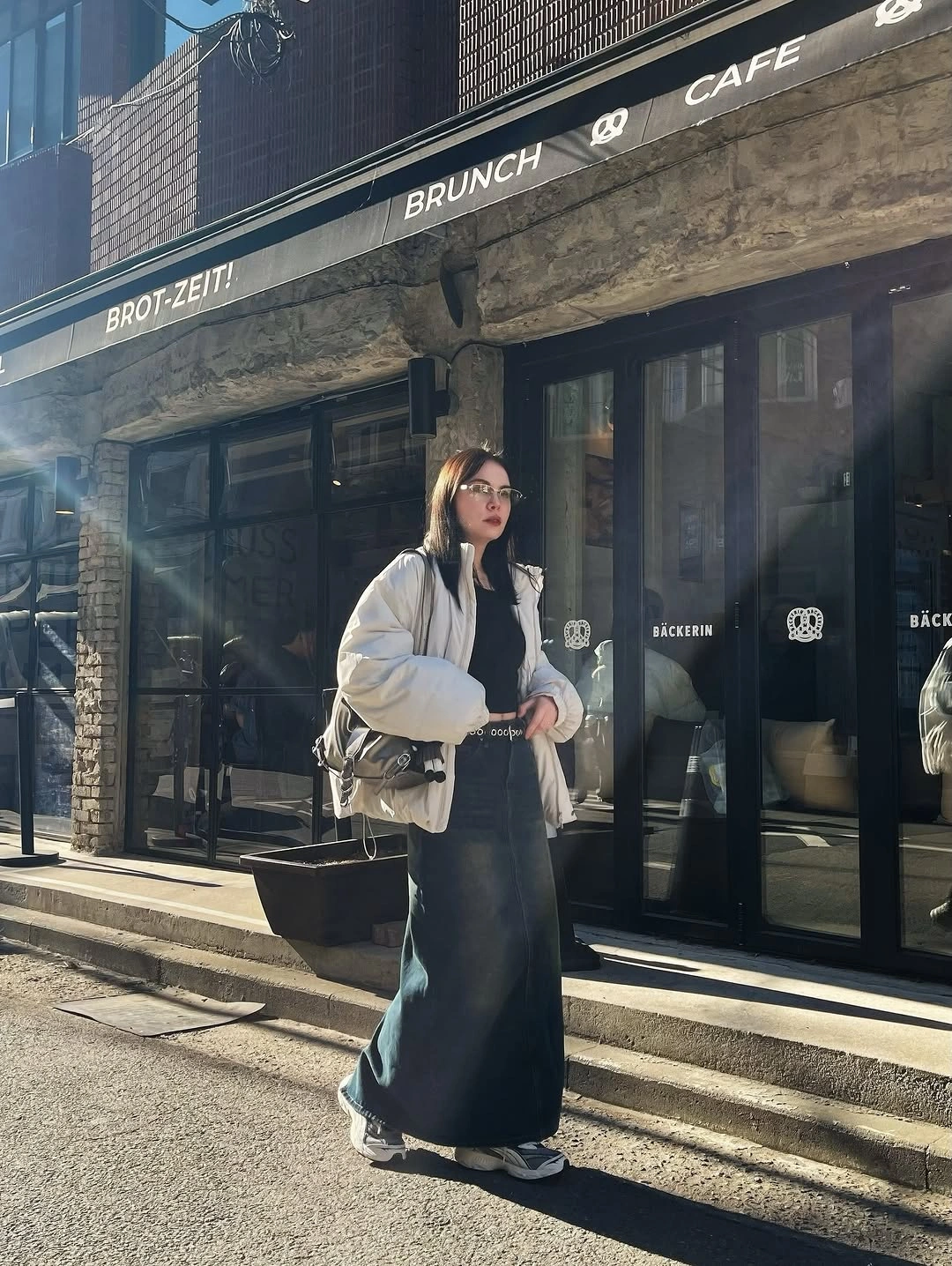 Light puffer-style jacket over black top, dark long skirt, and sneakers