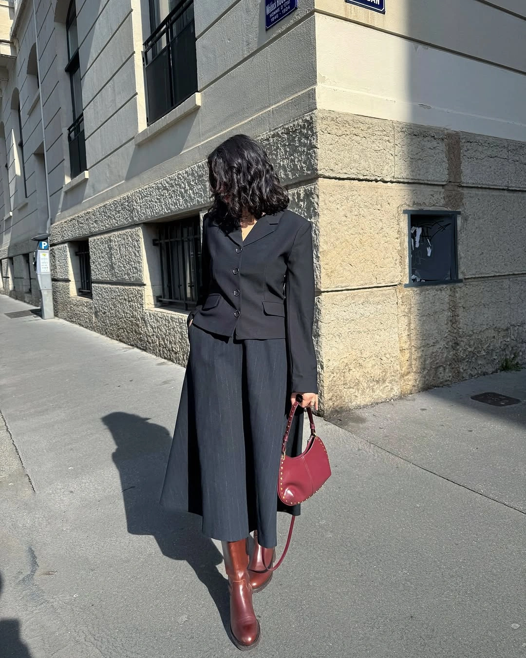 Black fitted jacket with dark pleated skirt-like piece and red-brown boots