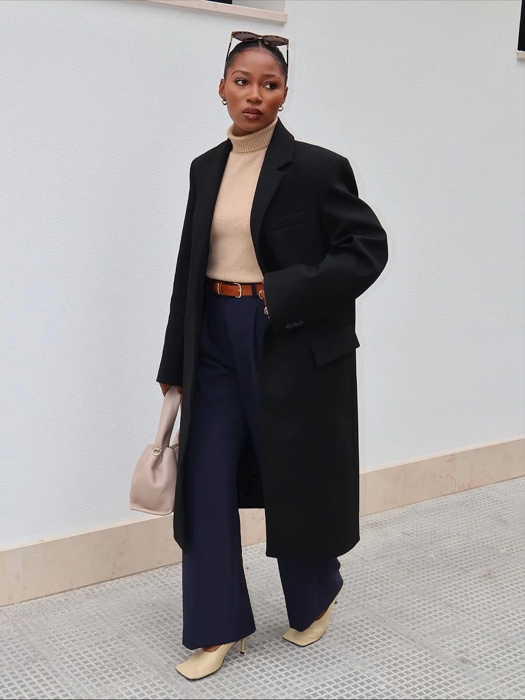 Long black coat over beige top navy trousers and pointed shoes