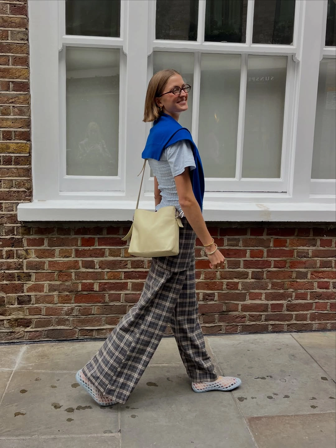 White T-shirt with cobalt sweater, plaid trousers, and pale bag