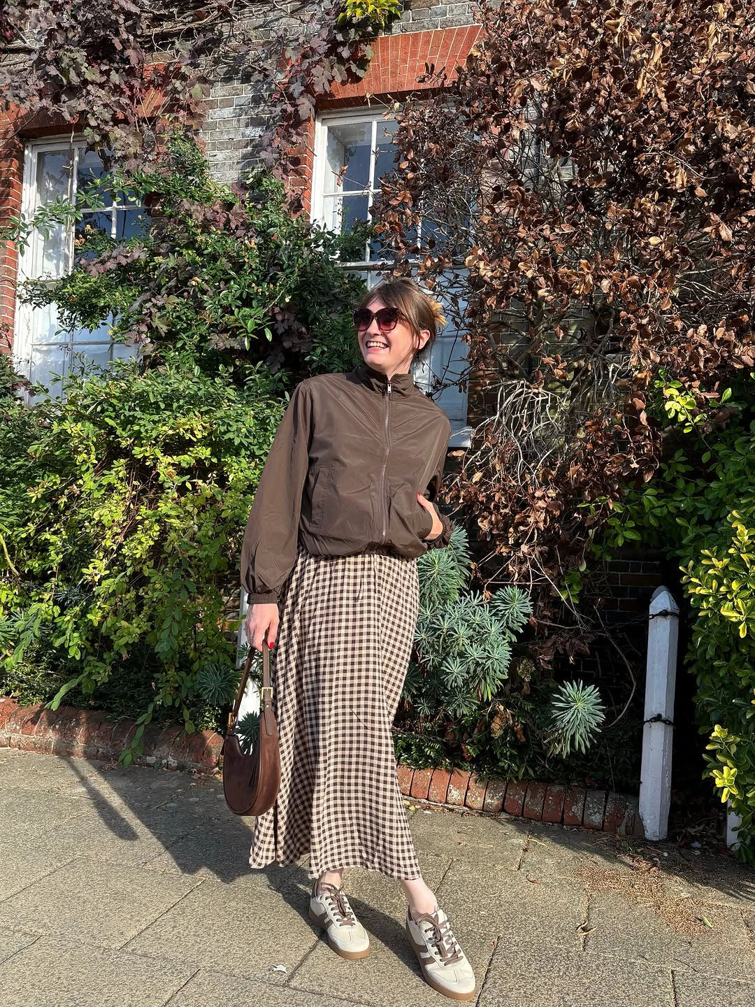 Brown jacket with checked midi skirt and gray-brown sneakers