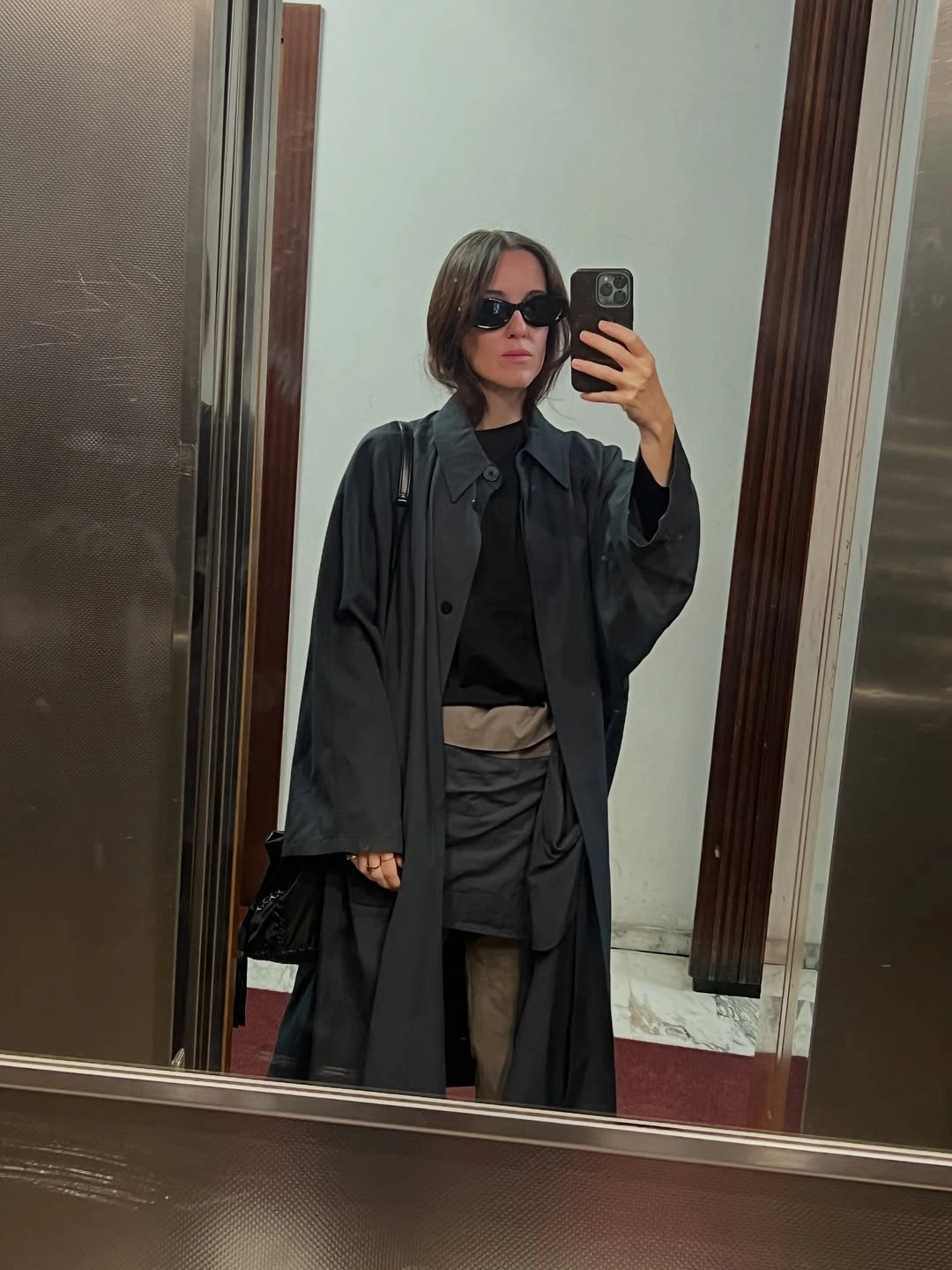 Long dark coat with mini skirt, sheer tights, and black bag
