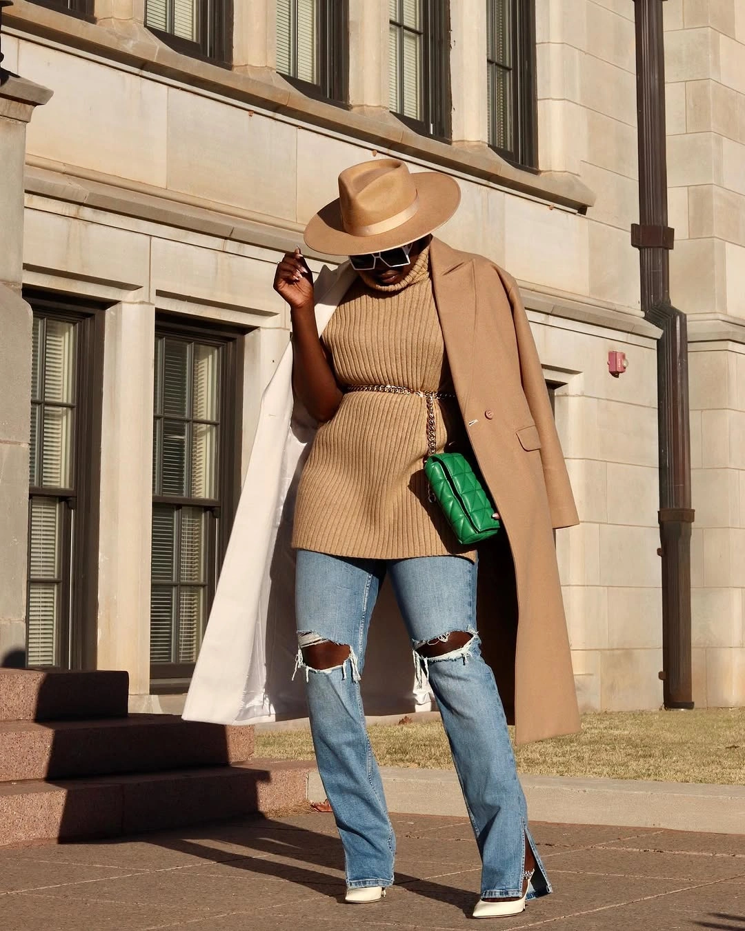 Woman in ripped light jeans, tan layers, wide-brim hat, and green bag