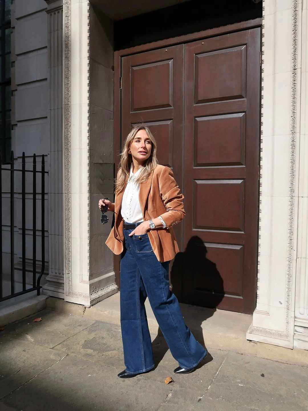 Woman in camel blazer, white top, and dark wide-leg jeans