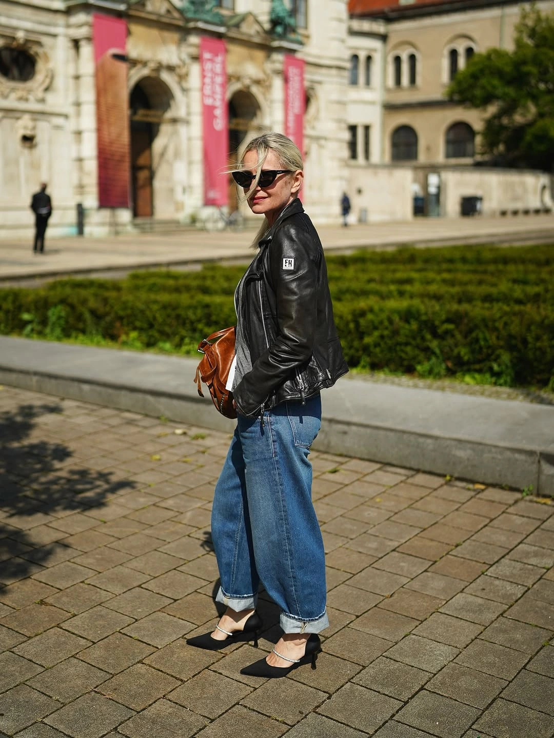 Woman in black jacket, cropped blue jeans, pointed shoes, and brown bag