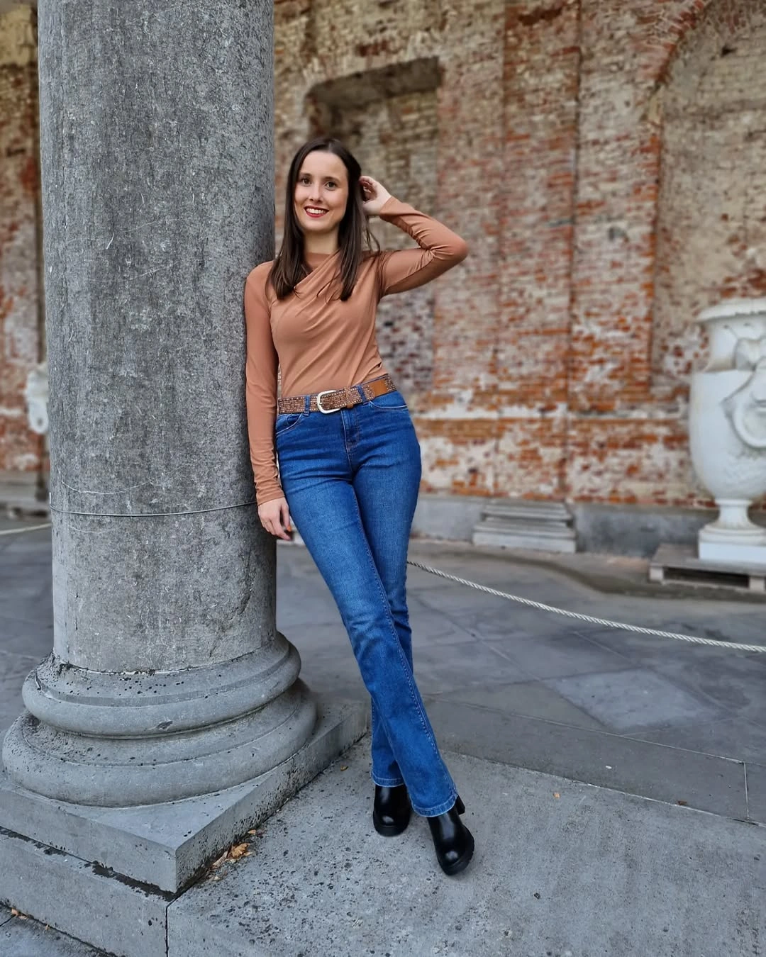 Woman in brown top, blue flared jeans, belt, and black boots