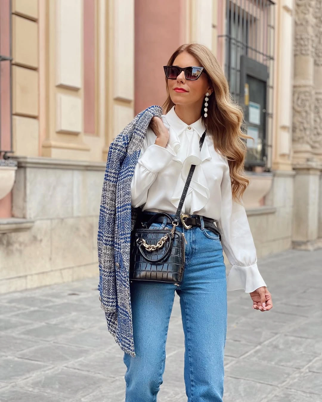 Woman in ruffled white blouse, blue jeans, jacket, and black bag