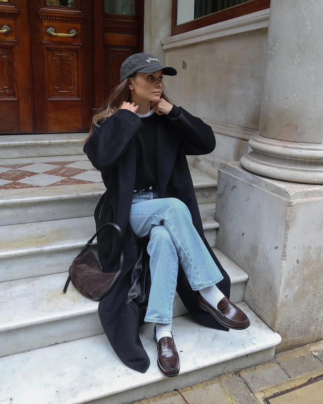 Woman in long dark layer, light jeans, white socks, and loafers