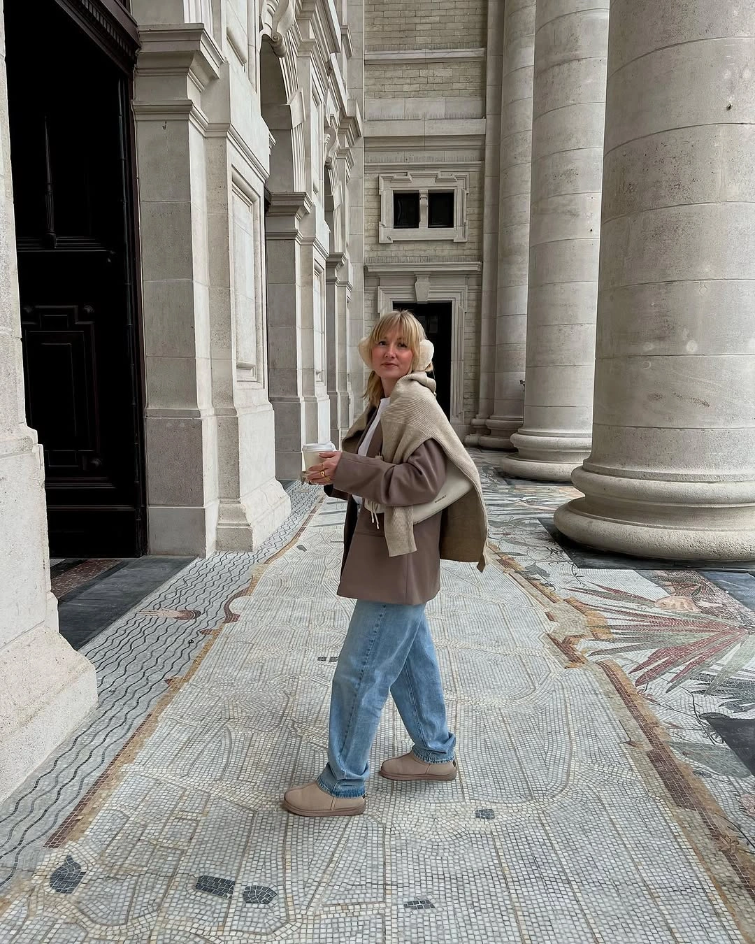 Woman in light jeans, taupe jacket, pale scarf, and beige shoes