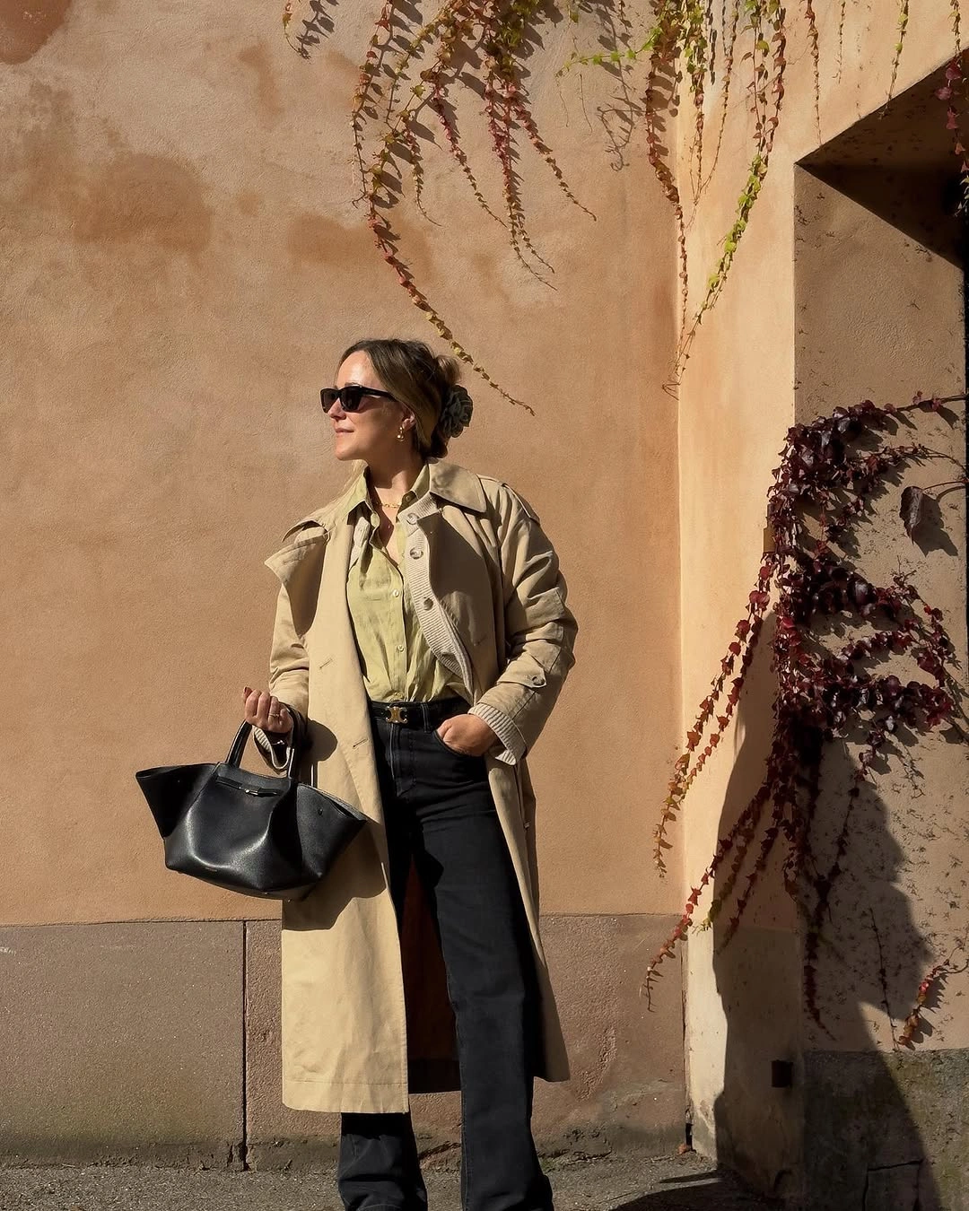 Woman in beige trench, olive shirt, black jeans, and handbag