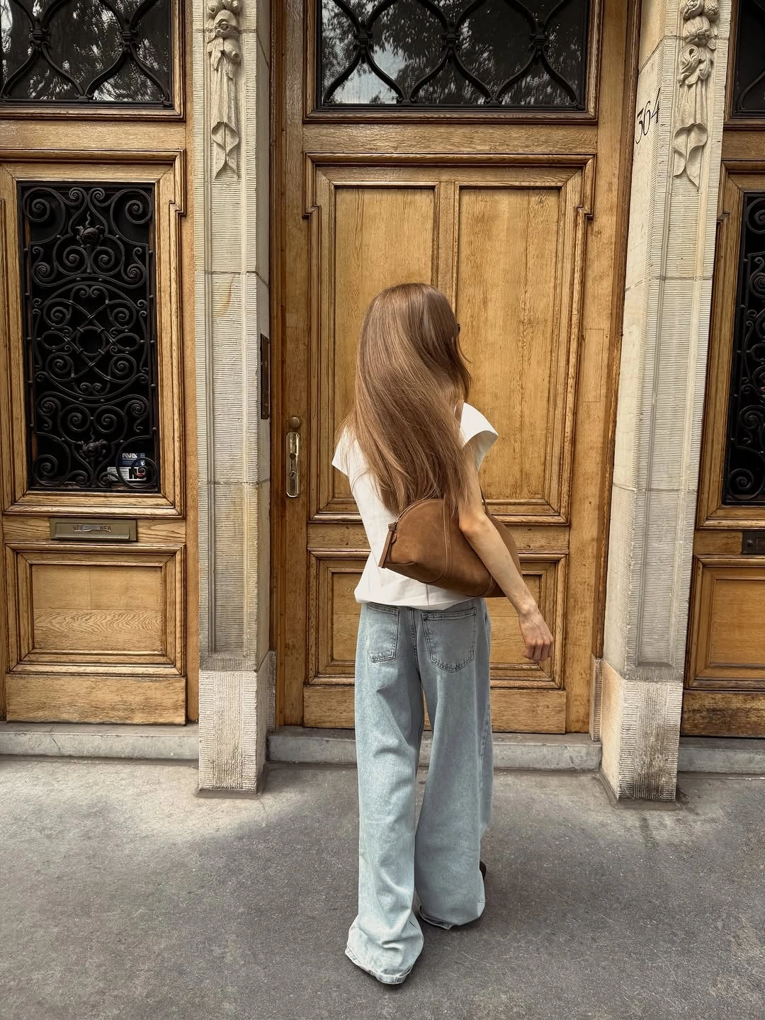 Woman in very wide pale jeans, white top, and brown bag