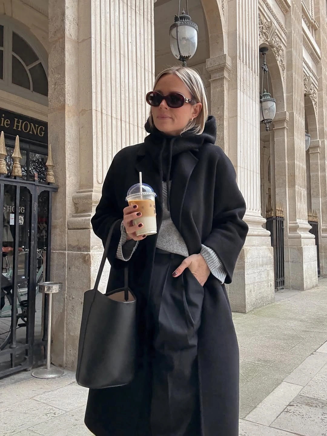 Oversized black coat with dark neck wrap, sunglasses, and large tote