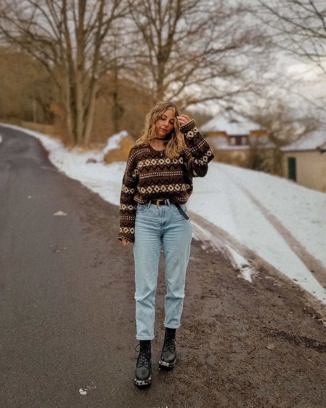 Woman wearing dark patterned sweater, light blue jeans, and black lace-up boots