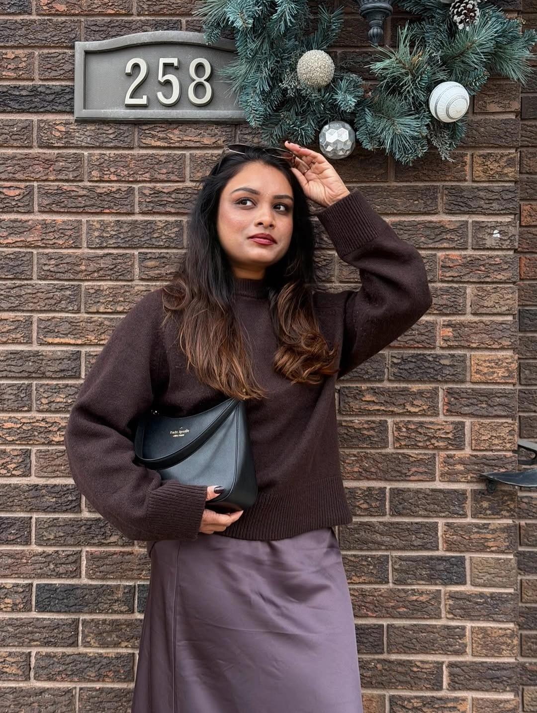 Woman wearing dark brown sweater, muted plum skirt, and black shoulder bag