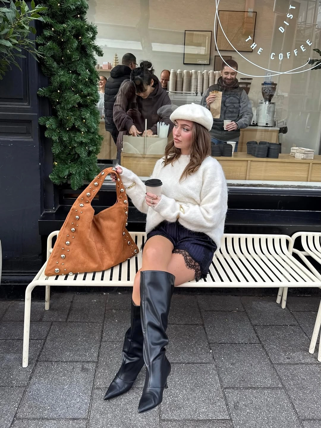 Woman in cream sweater, light hat, short dark bottoms, and tall boots